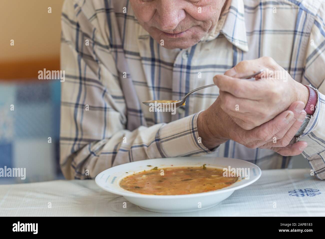 Älterer Mann mit Parkinsons Krankheit hält Löffel in beiden Händen. Stockfoto