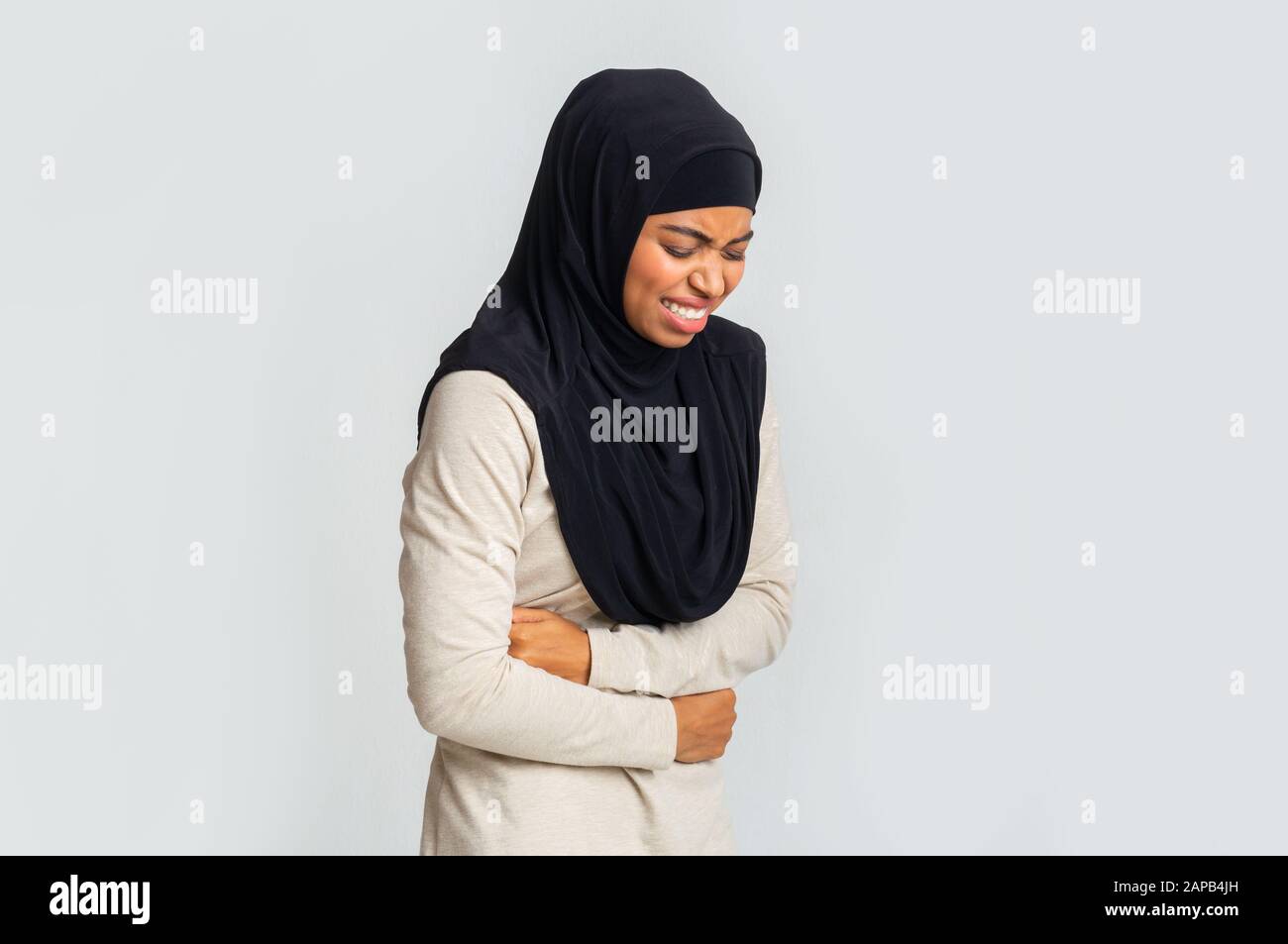 Schwarzes muslimisches Mädchen im Hijab, das an Bauchschmerzen leidet Stockfoto