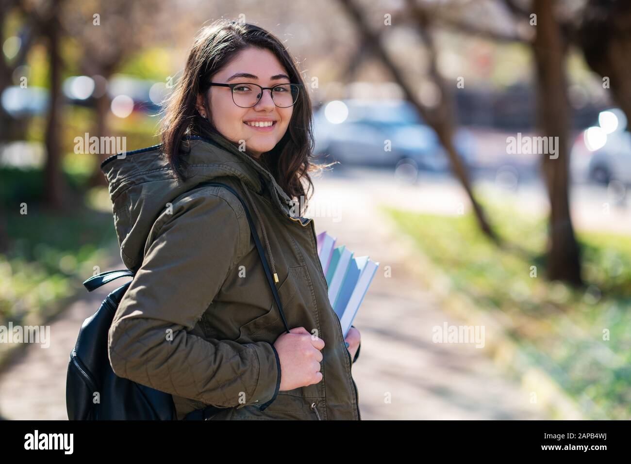Intellektuelles junges Mädchen bleibt und schaut zu jemandem in einem Park mit einigen Büchern in ihren Händen Stockfoto