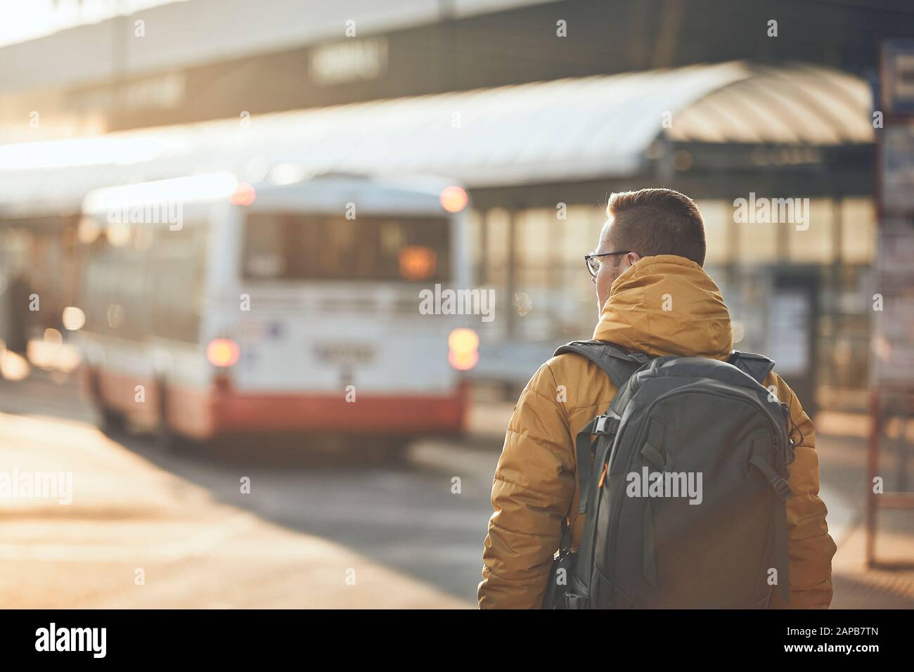 Junger Mann mit Rucksack, der zur Bushaltestelle geht. City Street bei goldenem Sonnenuntergang. Prag, Tschechien Stockfoto
