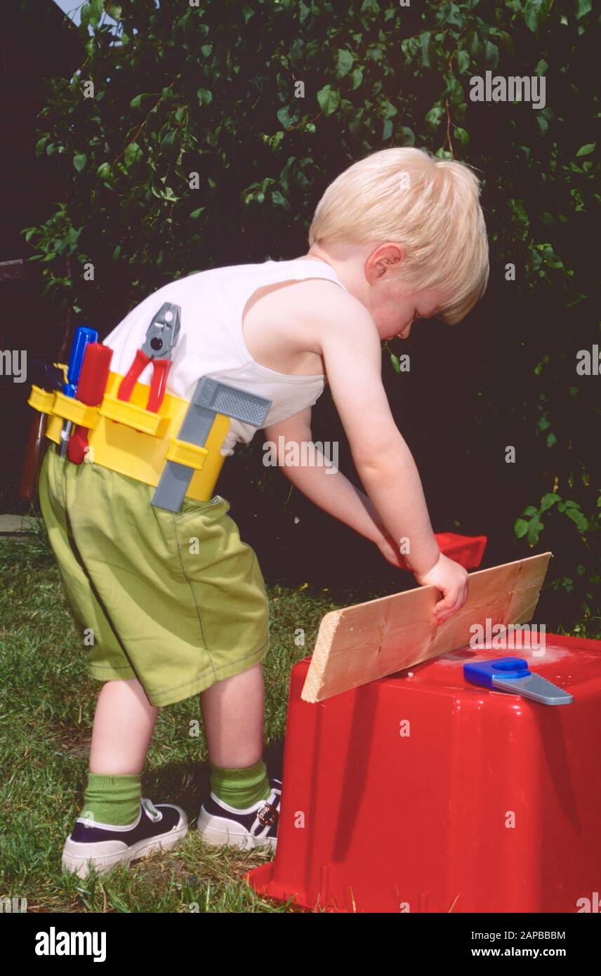 Kleiner Junge mit Spielgeräten, die vorgeben, Zimmermann zu sein, mit Weste auf, Sägen und Planen Stockfoto