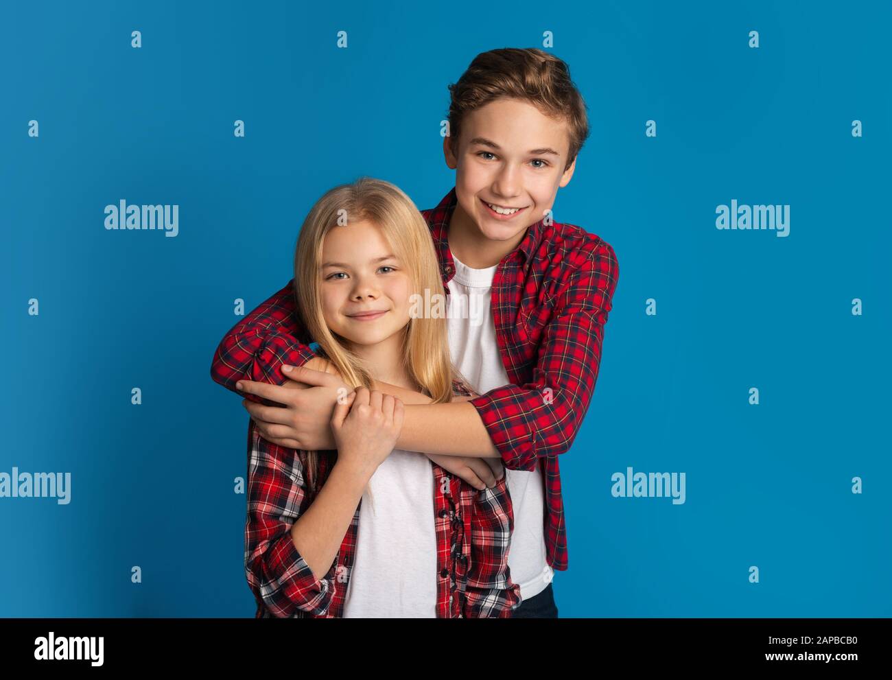 Glückliche Geschwister, Bruder und Schwester umarmen und posieren über blauem Hintergrund Stockfoto
