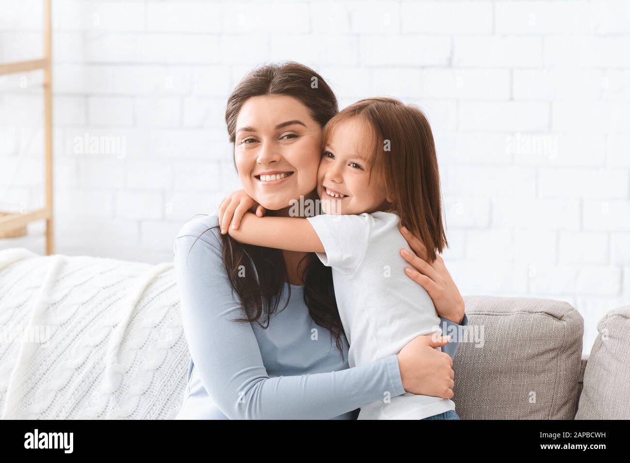 Porträt der fröhlichen Mutter und der kleinen Tochter, die sich zu Hause umarmt Stockfoto
