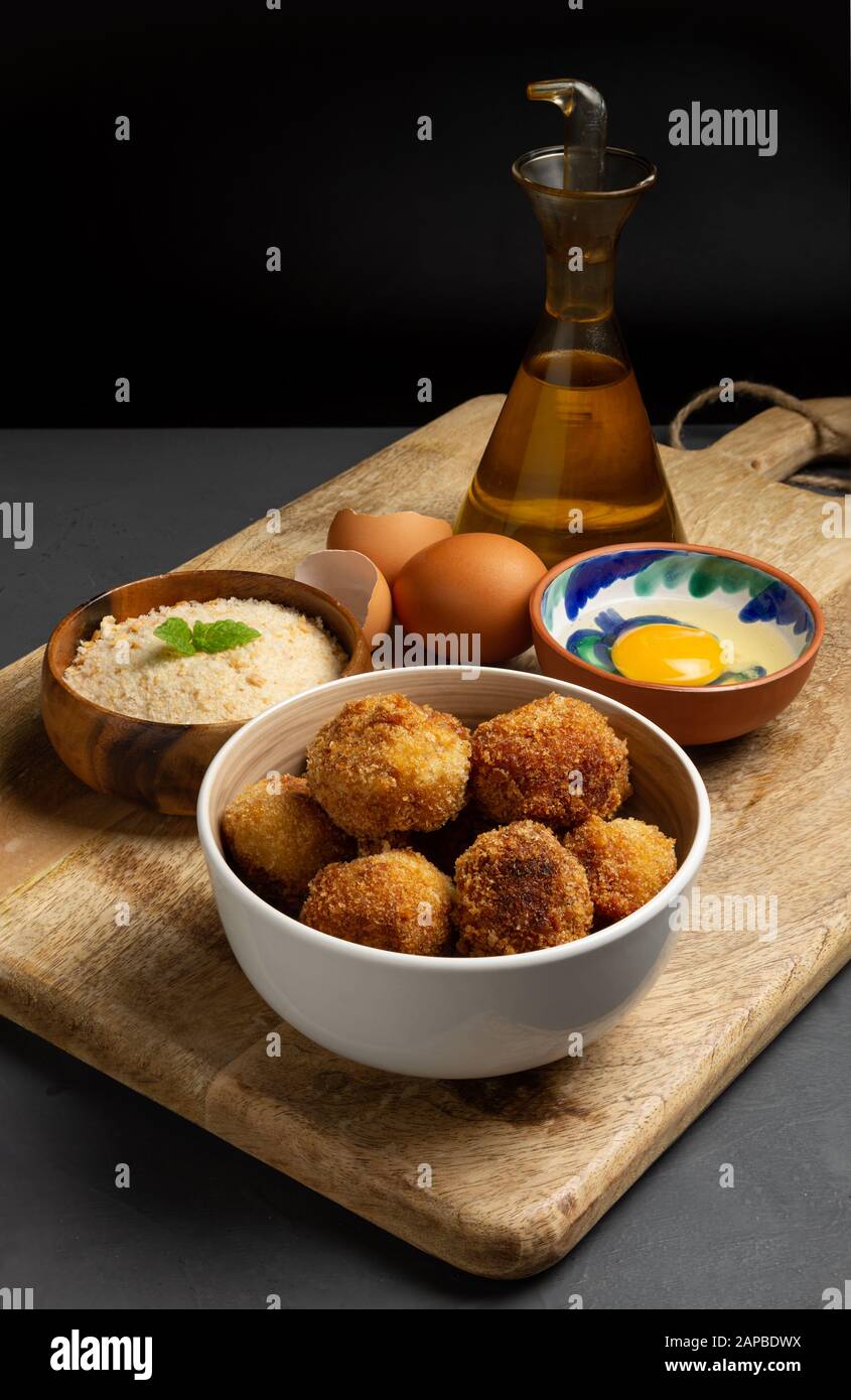 Hausgemachte Kroketten mit ihren Zutaten, dunkler rustikaler Hintergrund mit Platz für Kopien, gestreiftes Brot, Ei, Olivenöl Stockfoto