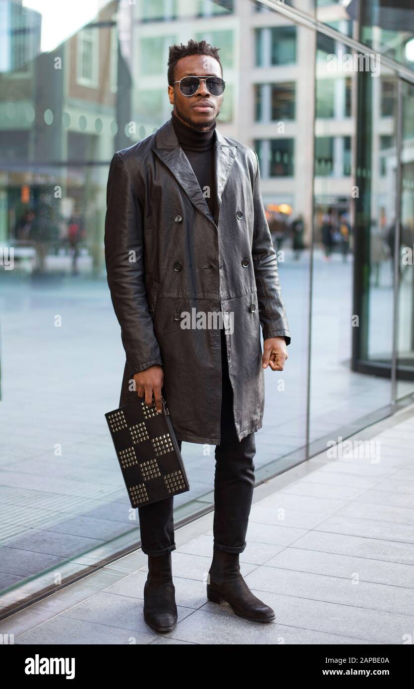 Ganzkörper-Straßenporträt von stilvollem, gut aussehenden schwarzen Mann mit Sonnenbrille und schwarzem Ledermantel. Instagram Mode-Blogger schauen mit MR Stockfoto