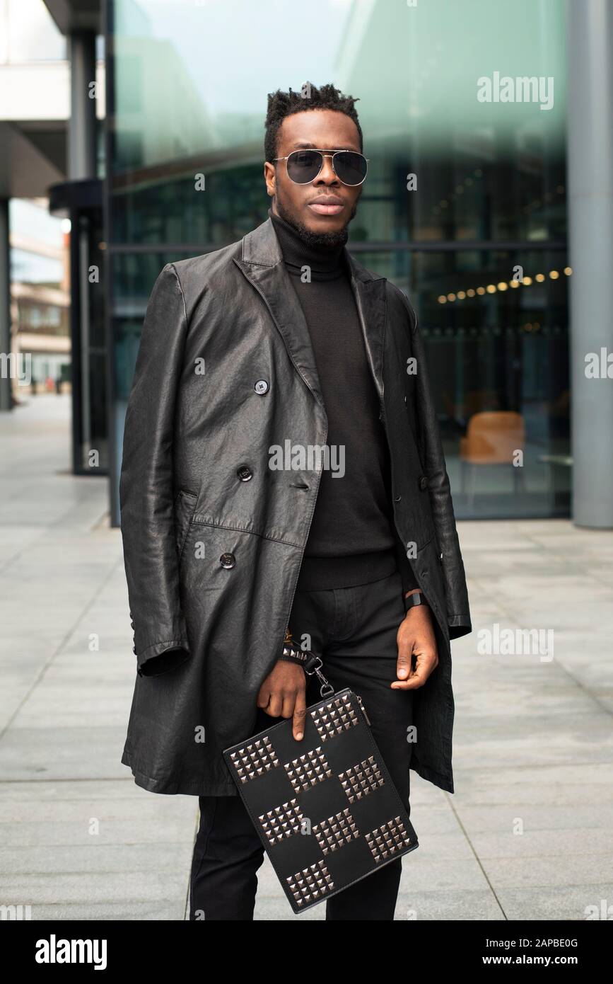 Straßenporträt von stilvollem, gut aussehenden schwarzen Mann mit Sonnenbrille und schwarzem Trenchcoat aus Leder. Instagram Mode-Blogger sehen mit MR-Model-Release aus Stockfoto
