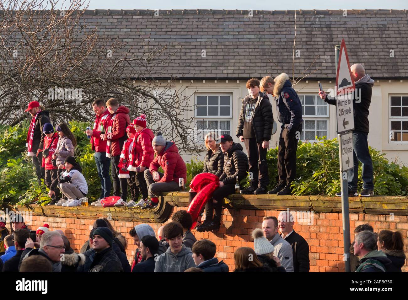 Kinder und Erwachsene, die LFC-Farben tragen, stehen an einer Wand und warten darauf, den Teamtrainer von Anfield Liverpool zu begrüßen. Stockfoto