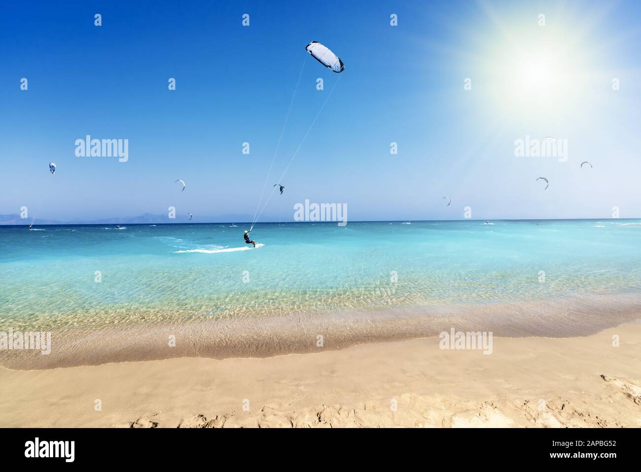 Kitesurfer reiten auf Wellen am Strand in der ägetischen See, blauer Himmel und Sonnenstrahlen (Rhodos, Griechenland) Stockfoto