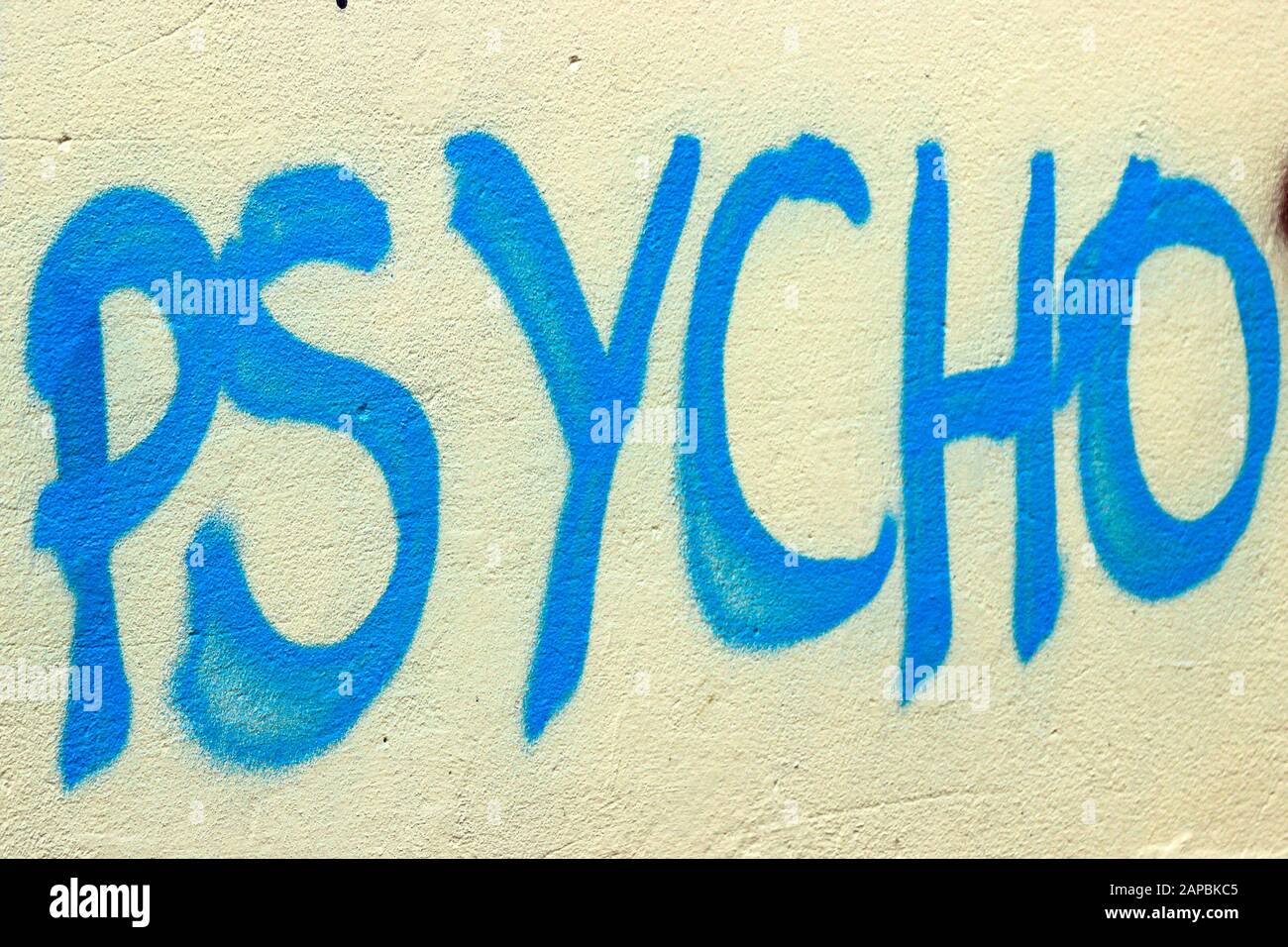 Psycho - blauer Graffiti-Text an gelber Wand Stockfoto