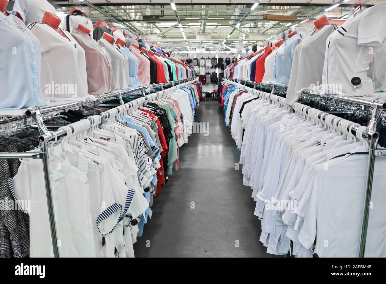 Weiße und helle Frauenshirts hängen an Bügeln und Mannequins in einem Bekleidungs- und Schuhgeschäft. Stockfoto