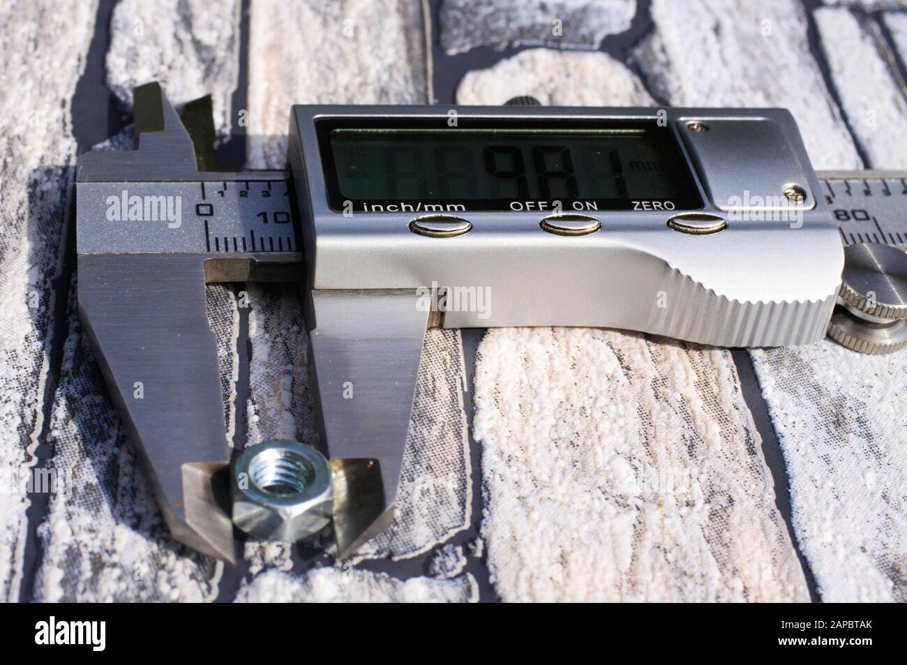 Makro-Nahaufnahme des elektronischen digitalen Bremssattels mit Mutter zwischen Messbacken, lcd-Anzeige und metrischer Skala. Steine Hintergrund. Stockfoto