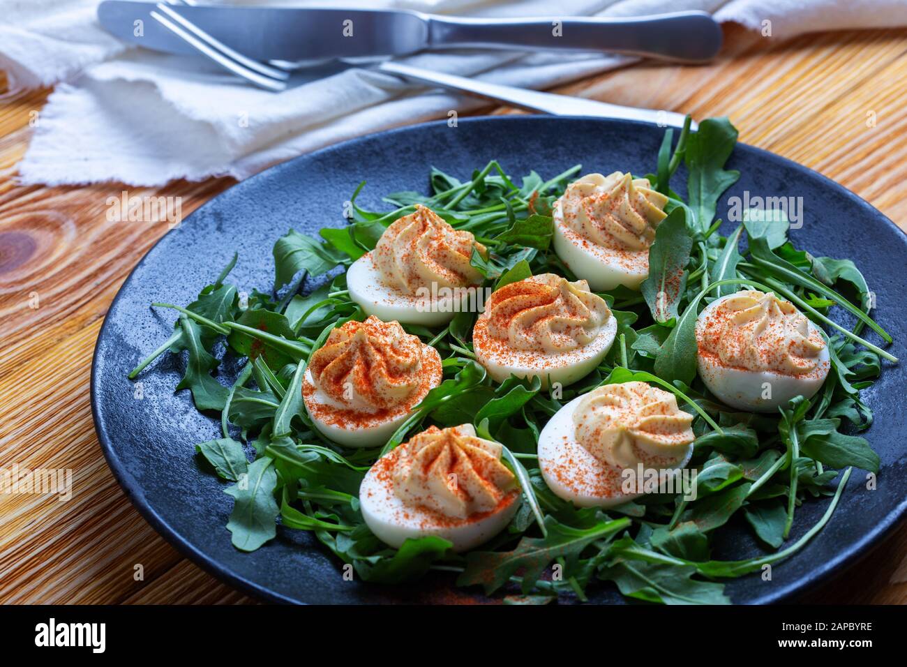 Eier mit Paprika auf frischen Nugulasalat in schwarzer ländlicher Platte auf Holztisch, gesunder vegetarischer Vorspeise oder Snack in der Nähe Stockfoto