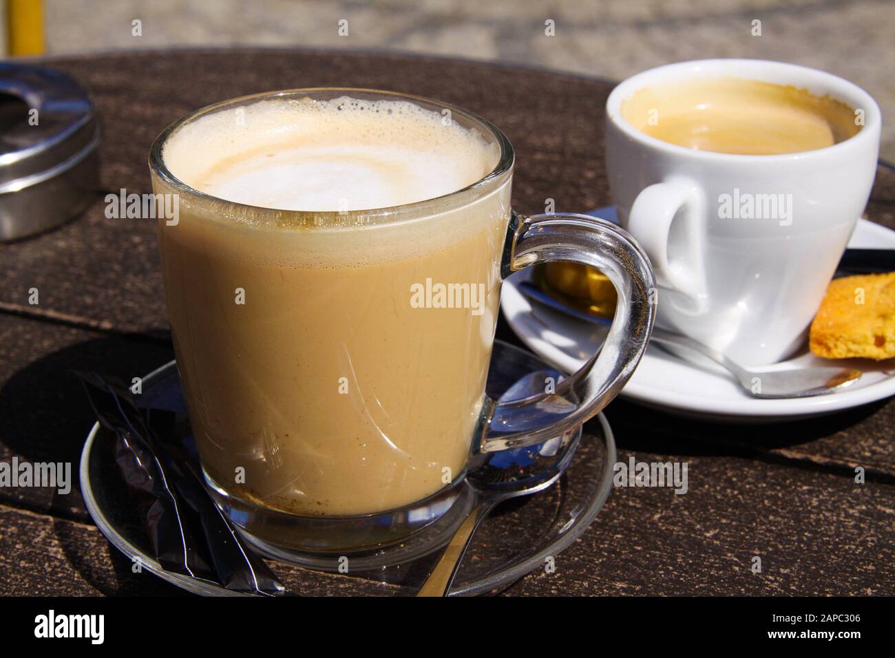 Nahaufnahme von isoliertem braunem holländischem Milchkaffee (Koffie verkeerd) in transparentem Glasbecher und weißem Espresso-Becher auf runder Holztafel Stockfoto