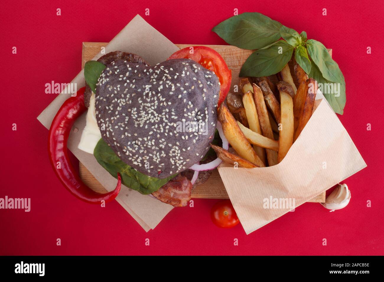 Herzförmige schwarz Hamburger, liebe Burger fast food Konzept, Valentines Tag überraschen Abendessen, roter Hintergrund, Ansicht von oben flach Stockfoto