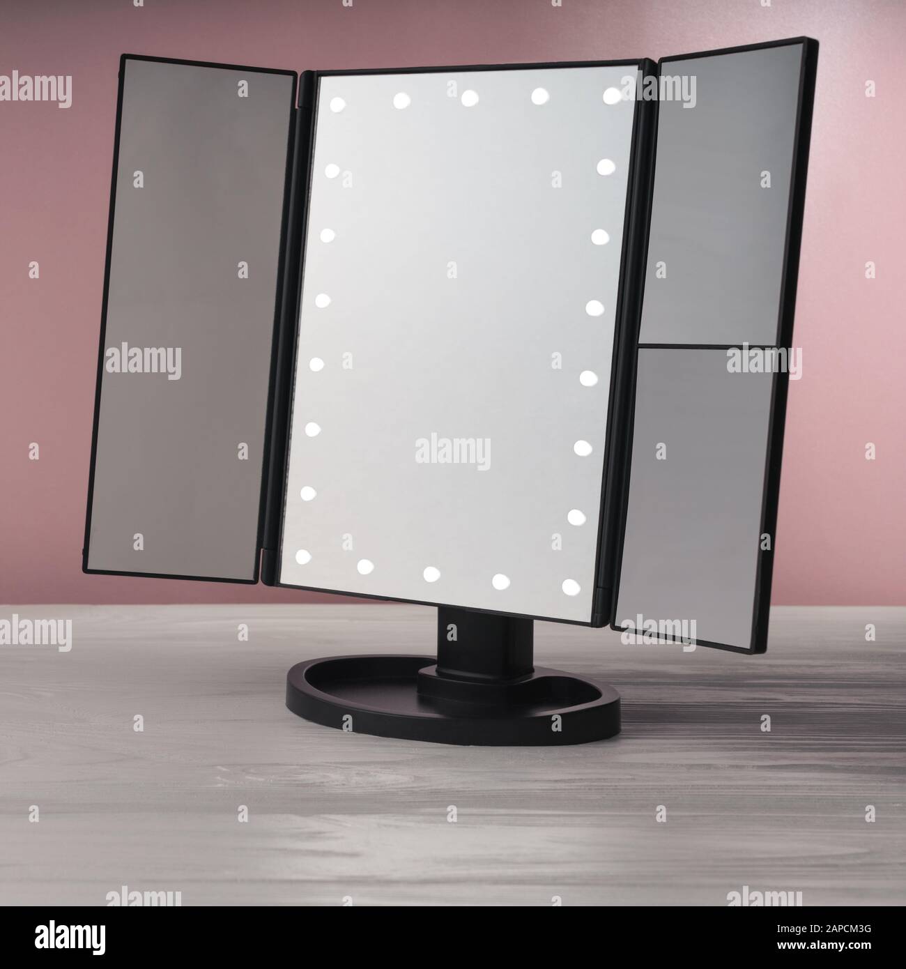 Schwarze LED-Schminke bilden einen Spiegel auf weißem Holztisch und einer rosafarbenen Wand Stockfoto