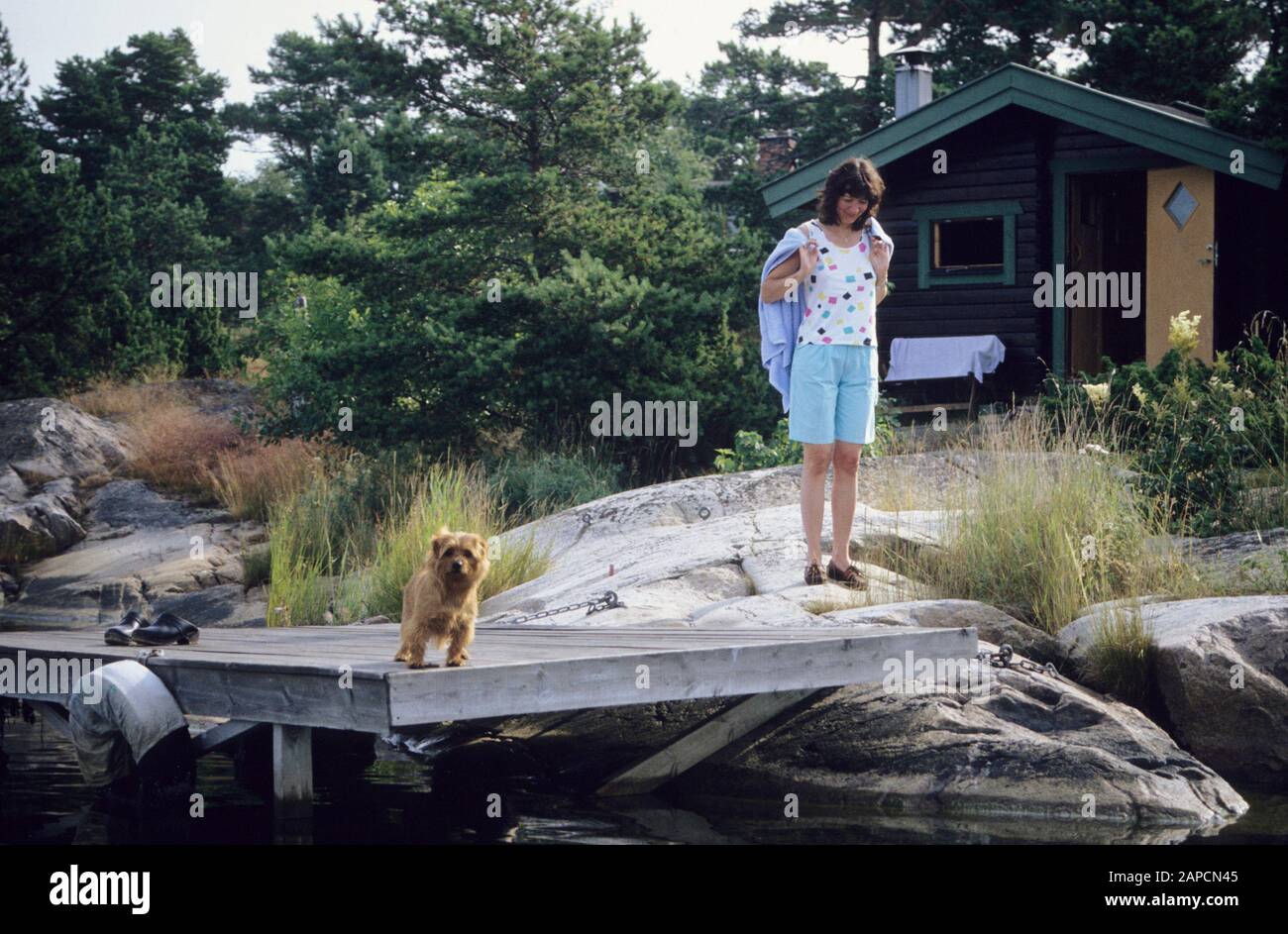 Frauen mit einem Norfolkterrier am Steg im Sommerhaus im Archipel Stockfoto