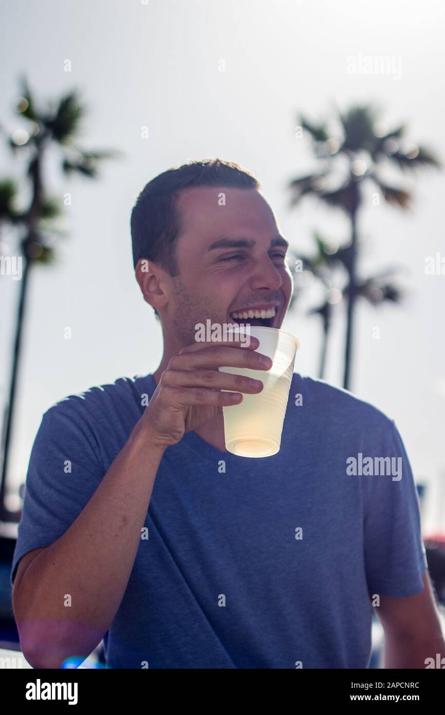 Männliches Modell, das aus einem Plastikbecher trinkt und in Los Angeles, Kalifornien, USA lacht Stockfoto