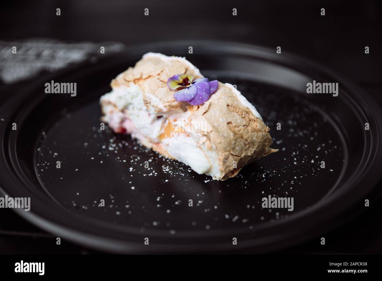 Lecker und frisch Meringue roll mit Sahne, bestreut mit Puderzucker, gekrönt mit einem Live-Blume. Stockfoto