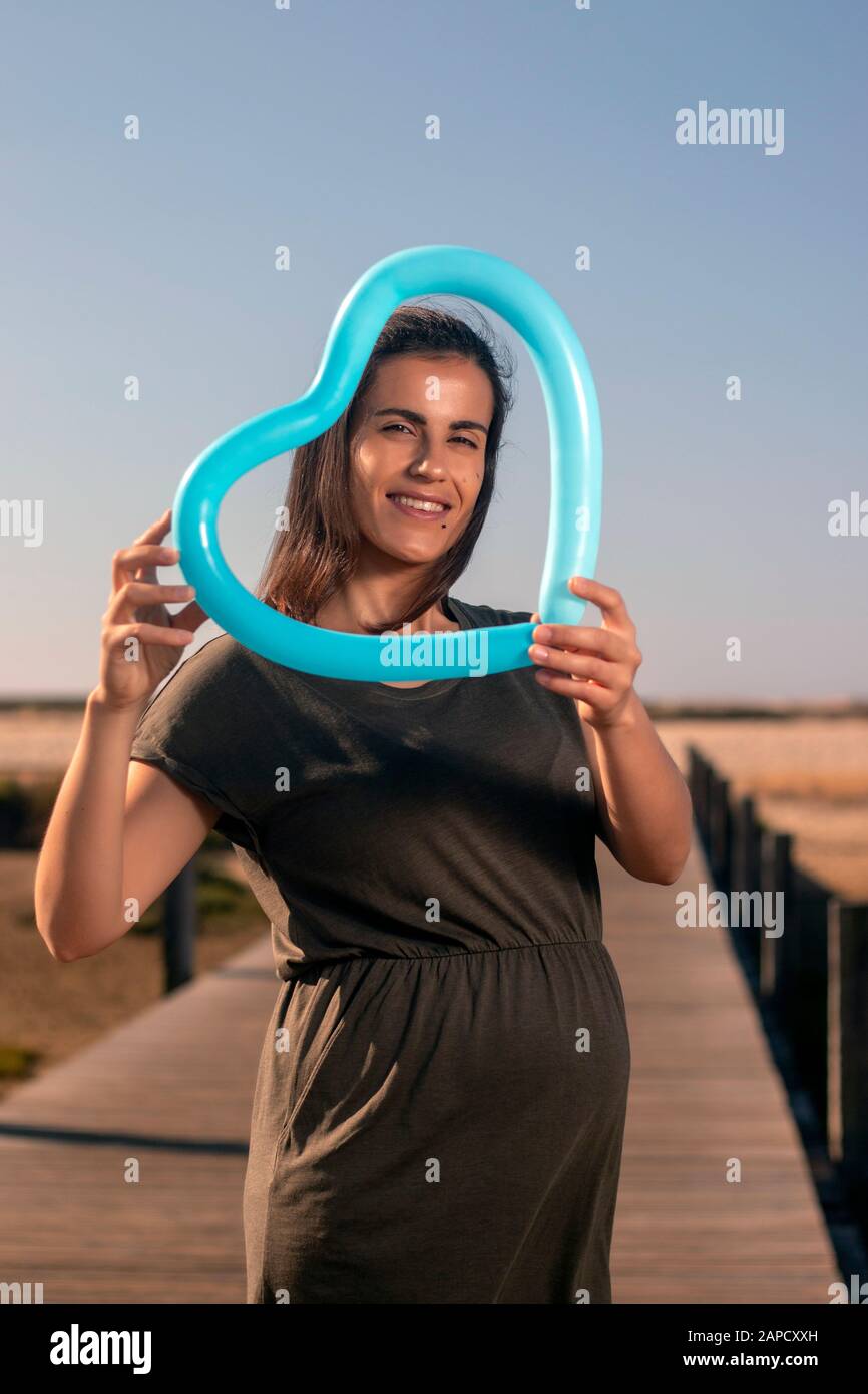Schwangere Frau posiert mit blauem Herzballon auf den Marschländern. Stockfoto