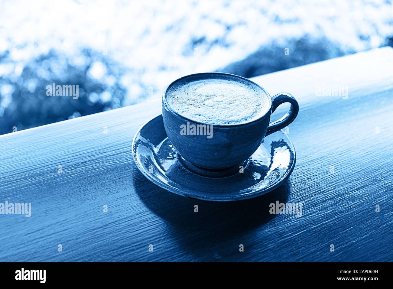 Farbe 2020 klassisch blau. Tasse Kaffee auf tropischem Hintergrund, blau eingefärbt. Stockfoto