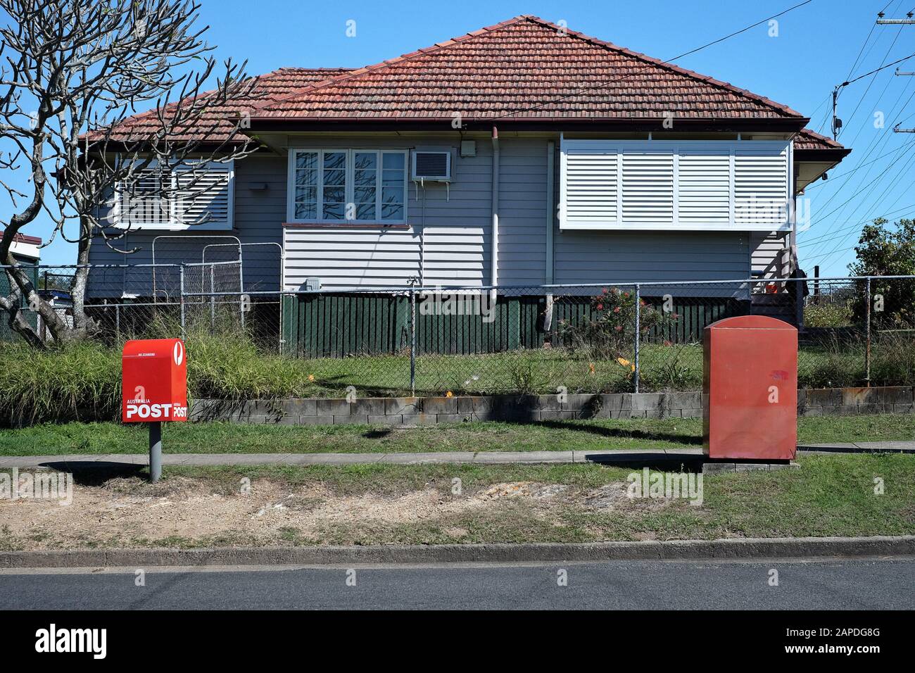 Zwei Rote Postboxen und ein originales Arbeiterhaus aus der Nachkriegszeit, rote Dachziegel, Flügelfenster, Wetterbrett auf niedrigen Baumstümpfen, in Carina, Brisbane Stockfoto