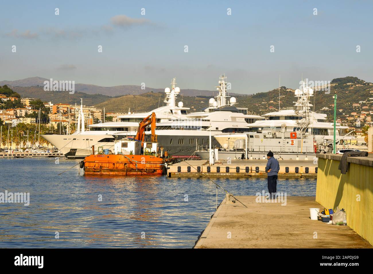 Blick auf den Touristenhafen von Porto Maurizio mit einem Fischer, der mit einem Stab am Kai angeln kann, und einer gefesterten Luxusyacht, Imperia, Ligurien, Italien Stockfoto