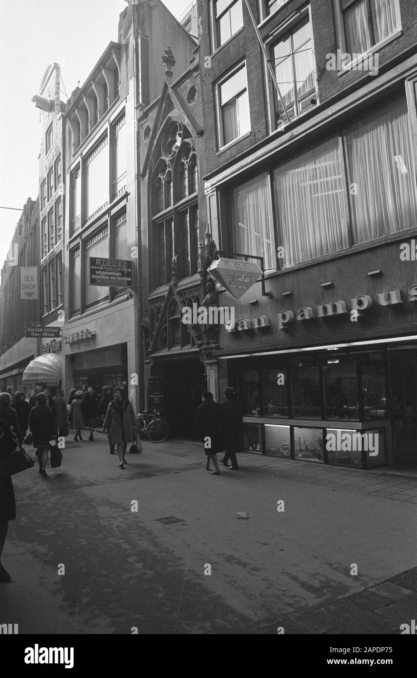 Kirchenbauten sind geschützt Beschreibung: Amsterdam, Kalverstraat. Eingang zum St. Petrus und Pauluskerk, genannt De Parrot zwischen den Schaufenstern mit Werbeschildern Datum: 28. Februar 1974 Ort: Amsterdam, Noord-Holland Schlüsselwörter: Architektur, Fassaden, Katholizität, Kirchenbauten, Neugotik, Portale, Stadtplastiken Stockfoto