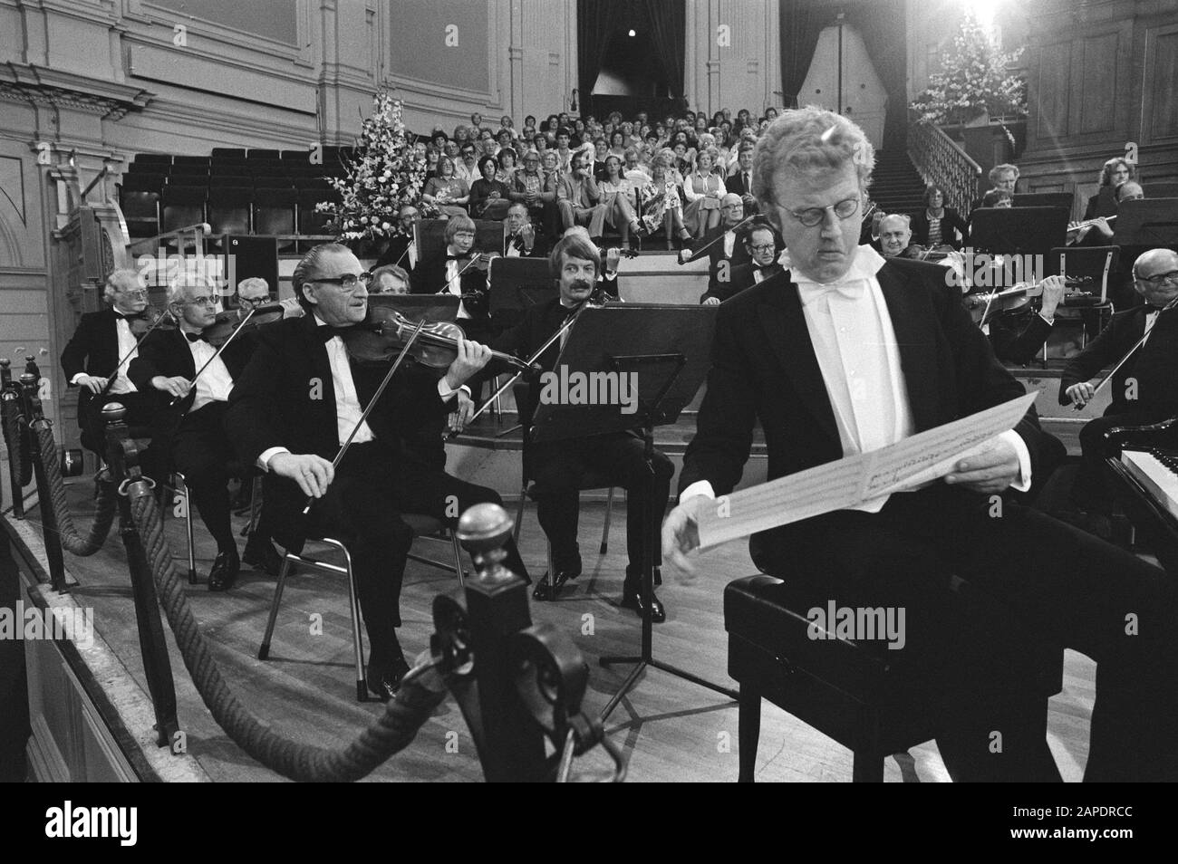 André van Duin im Concertgebouw für eine Filmaufnahme Beschreibung: André van Duin hinter dem Flügel, vor dem Orchester, auf der Bühne Anmerkung: Aufnahmen für den Film "Ich bin Joep Melon". André van Duin in der Rolle des Klaviertuner mit dem Traum, ein renommierter Konzertdirigent zu sein. Unter Mitwirkung des Concertgebouw Orchesters. Datum: 19.August 1981 Ort: Amsterdam, Noord-Holland Schlagwörter: Künstler, Film, Musiker, Orchester persönlicher Name: Duin, André van Stockfoto