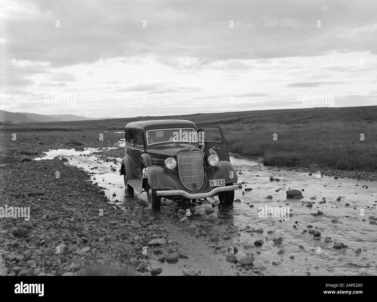 Beschreibung von Island: Auto, das durch das Bett eines flachen Stroms fährt Datum: 1934 Ort: Island Schlagwörter: Autos, Bäche, Landschaften, Felsen Stockfoto