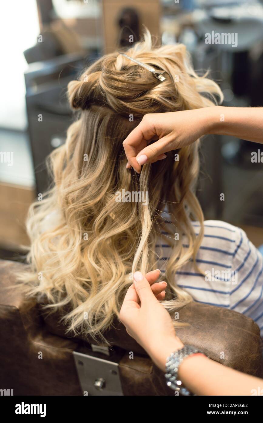 Der Friseur kreiert Locken und wellenförmige Haare in der Blondine. Die Hände des Friseursalons locken beim Kunden. Stockfoto