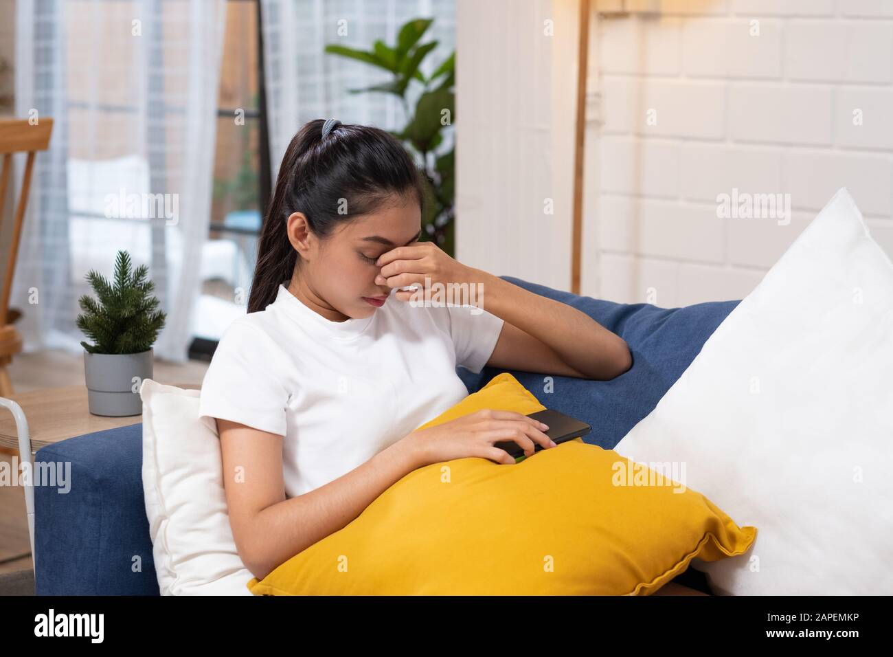 Junge asianerin, die Stress und geschlossene Augen spürt, leidet unter Kopfbedeckung auf dem Sofa im Wohnzimmer, müde Büroangestellte massa Stockfoto