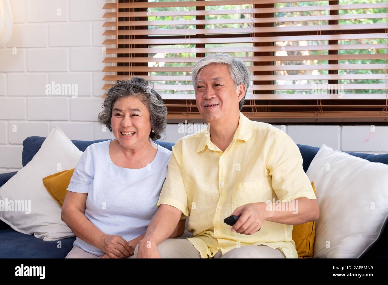 Älteres Asiatisches Paar sitzt auf dem Sofa und verwendet die Fernbedienung, um den Sender zu wechseln und Fernsehen im Wohnzimmer zu Hause zu sehen. Stockfoto