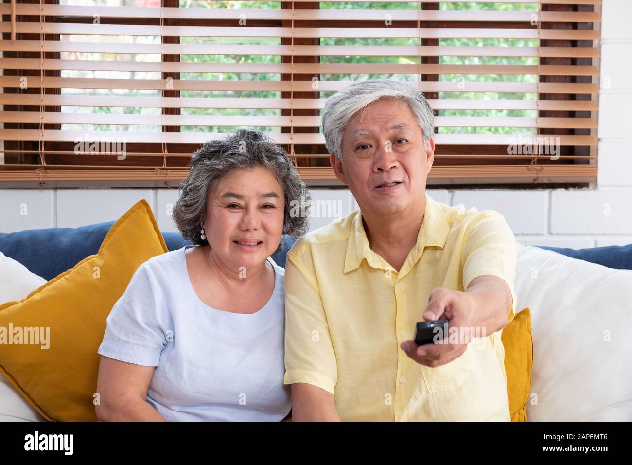 Älteres Asiatisches Paar sitzt auf dem Sofa und verwendet die Fernbedienung, um den Sender zu wechseln und Fernsehen im Wohnzimmer zu Hause zu sehen Stockfoto