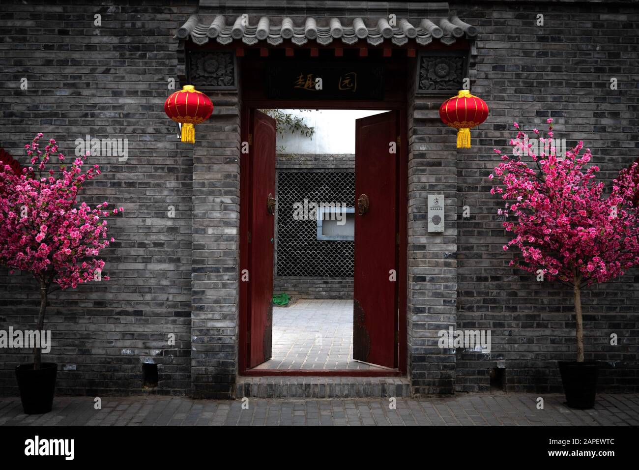 Rote Tür und Tor, die Eingang zu einem privaten Innenhof und einem Wohnhaus in einer Hutong-Gasse in Peking, China, bieten. Dekoriert für das chinesische Neujahr Stockfoto