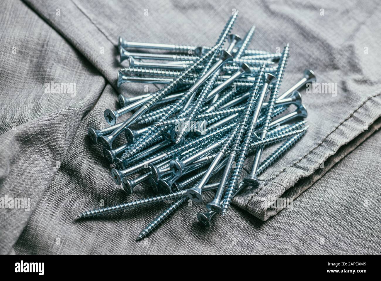 Eine Handvoll metallischer Selbstschneiderschrauben liegt vor dem Hintergrund eines alten Denimstoffs. Selektives Fokusmakro mit flachem Freiheitsgrad. Stockfoto