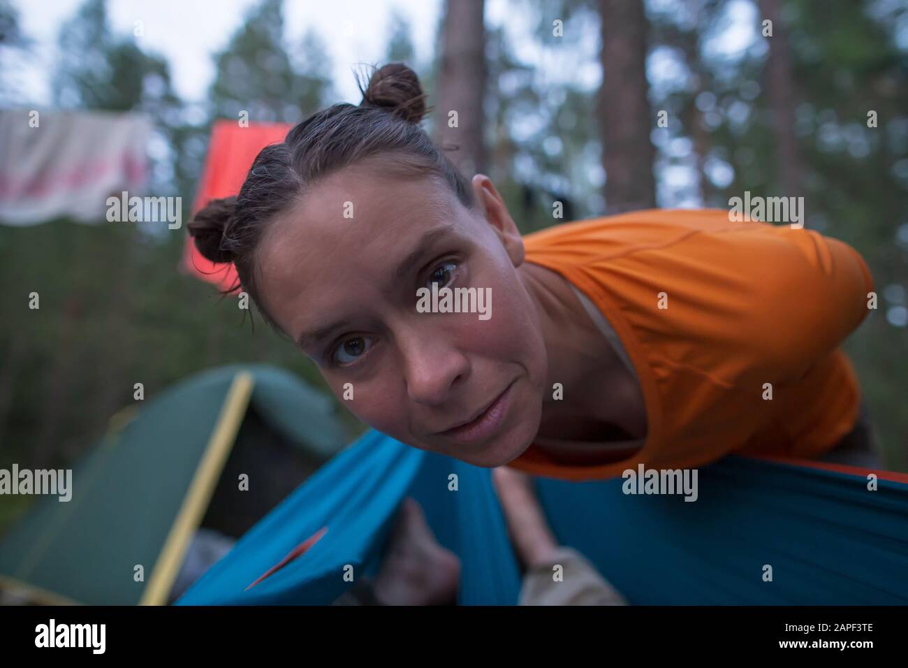 Neugierige Frau mit gebräuntem Gesicht und einer lustigen Frisur blickte in eine Hängematte und ihr Gesicht stand im Camp nahe der Kamera. Stockfoto