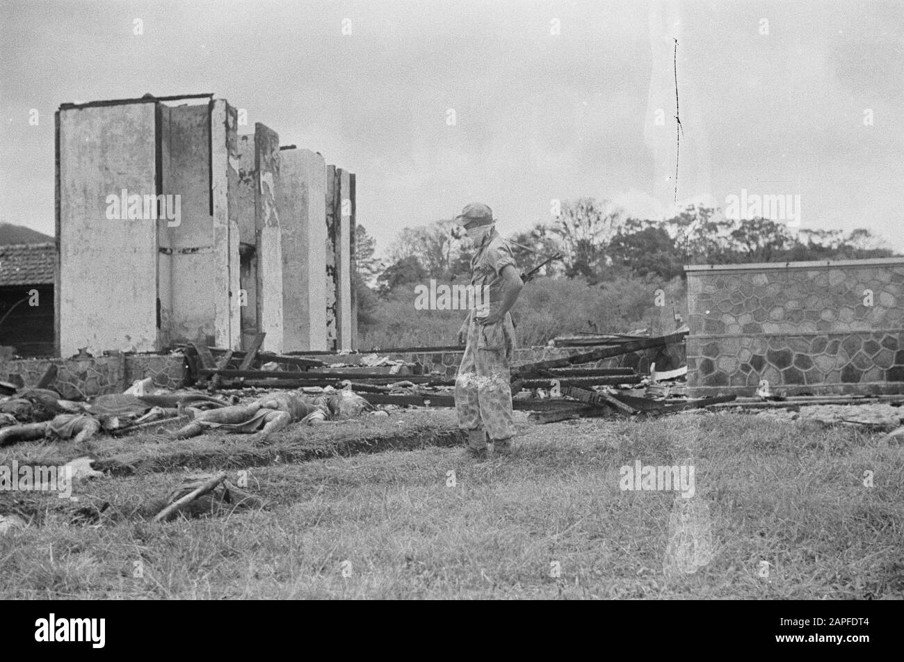 Brastagi. Bei ihrer Ankunft in Brastagi machten unsere Truppen einen lauteren Fund. In einem Massengrabmal wurden 18 verstümmelte Körper gefunden. Anderswo im Dorf wurden 40 schrecklich verstümmelte Leichen anderer Opfer des TNI Annotation gefunden: Soldat mit Tuch um den Mund steht in der Nähe eines ausgebrannten Gebäudes. Es gibt Überreste Datum: August 1947 Ort: Indonesien, Niederländisch-Ostindien Stockfoto