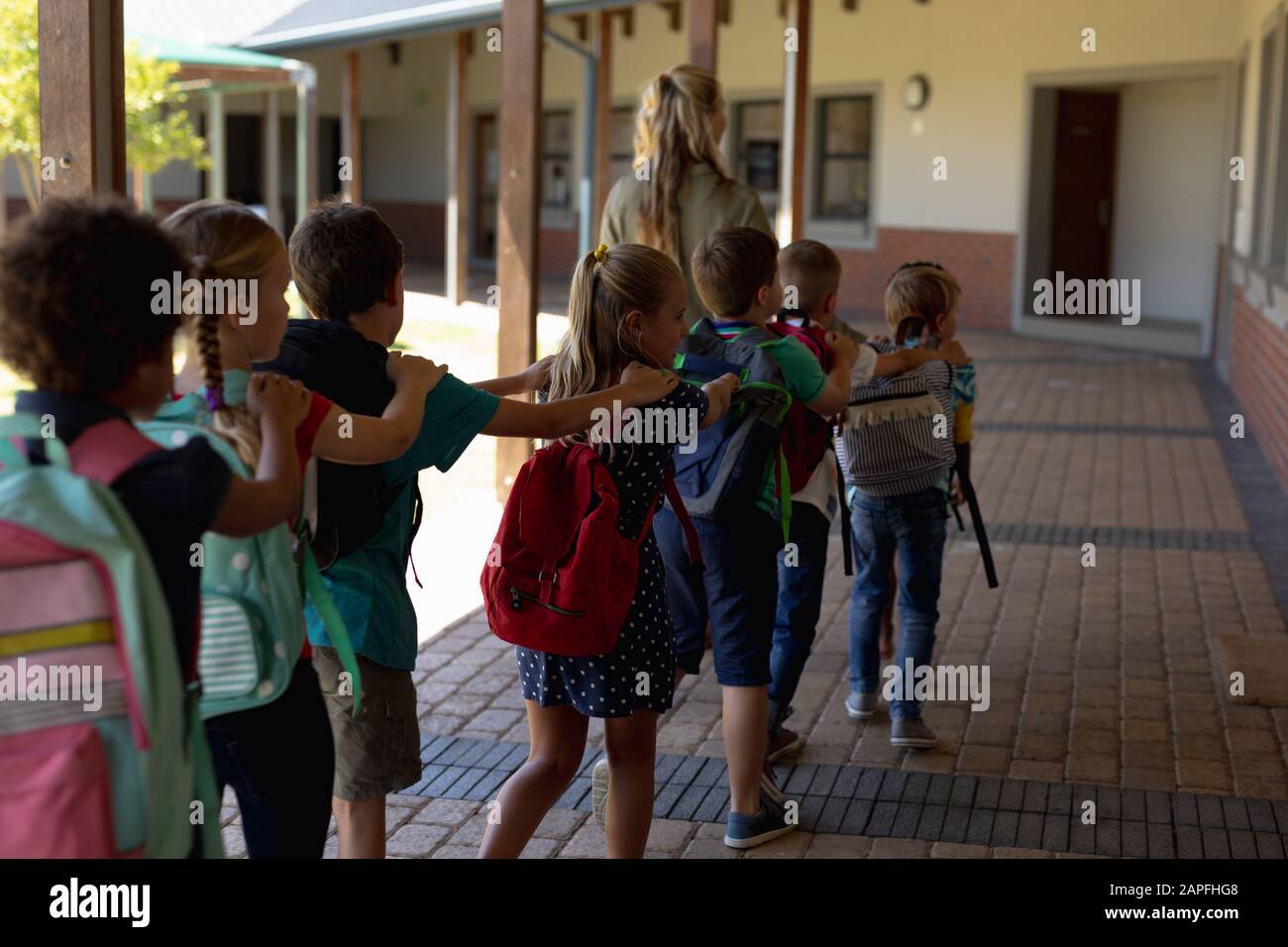 Lehrerin mit Schulkindergruppe, die einen Außenkorridor an einer Grundschule geht Stockfoto