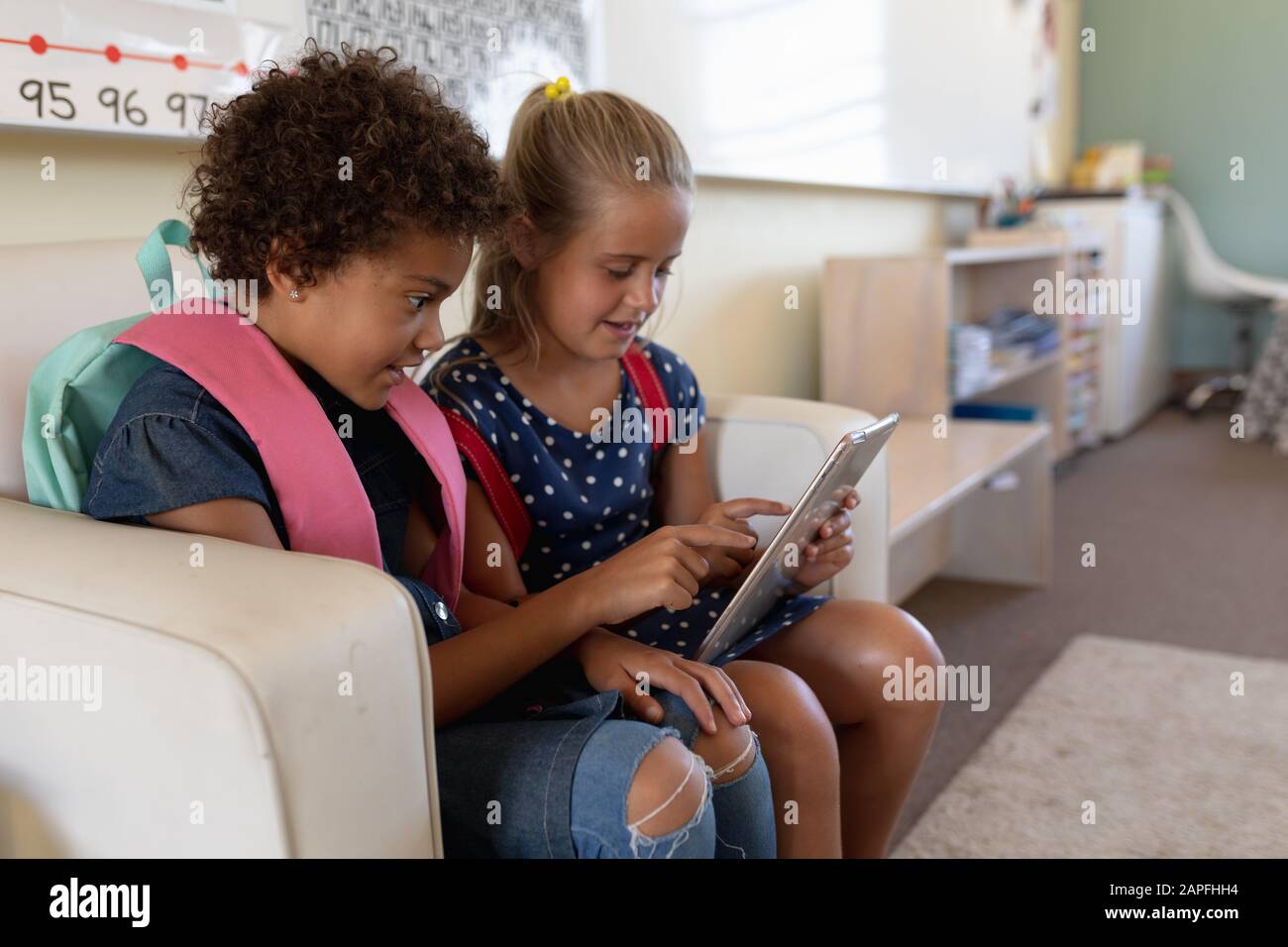 Schulmädchen schauen gemeinsam in einem Klassenzimmer der Grundschule auf einen Tablet-Computer Stockfoto