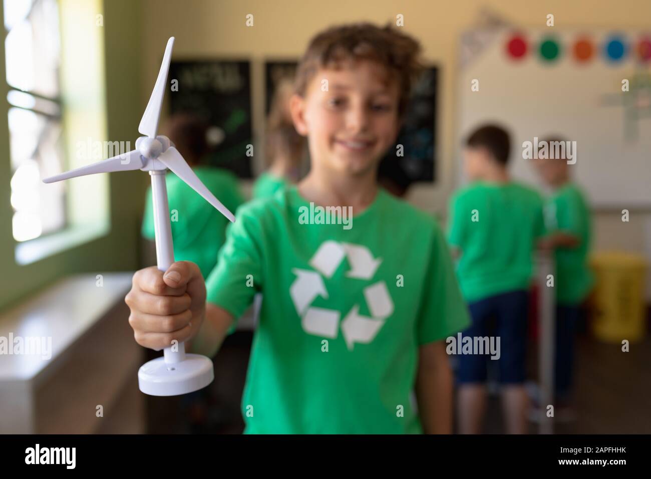 Schuljunge, die ein grünes T-Shirt mit einem weißen Recycling-Logo darauf tragen und winddrübe im Miniaturformat halten Stockfoto