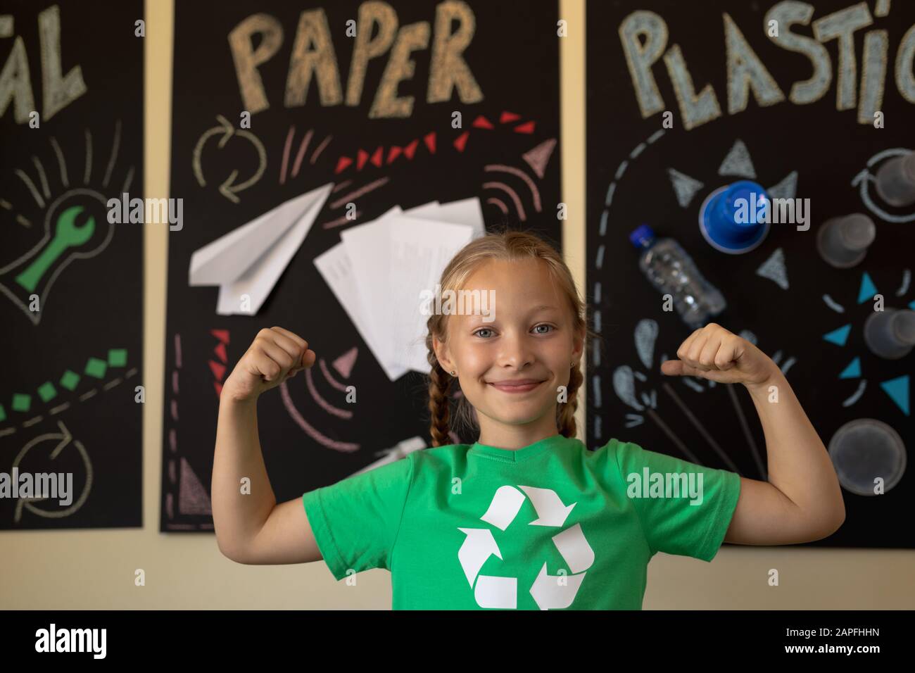 Schulmädchen trägt ein grünes T-Shirt mit einem weißen Recycling-Logo darauf und beugt ihre Bizeps Stockfoto