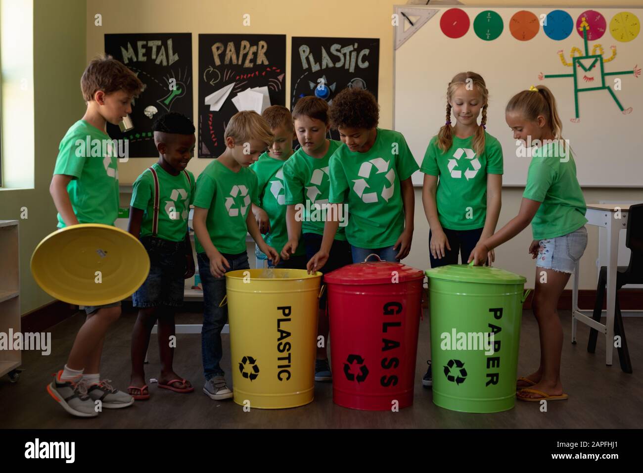 Gruppe von Schulkindern, die farbcodierte Recyclingbehälter und -Beutel in einem Klassenklasso der Grundschule halten Stockfoto