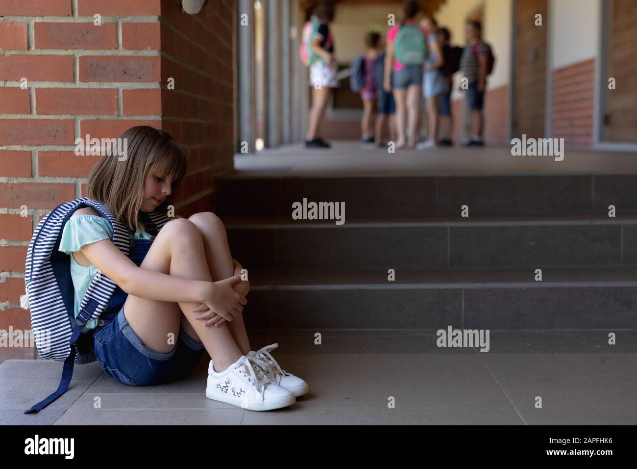 Allein auf dem Schulhof der Grundschule sitzt Schulmädchen auf dem Boden Stockfoto