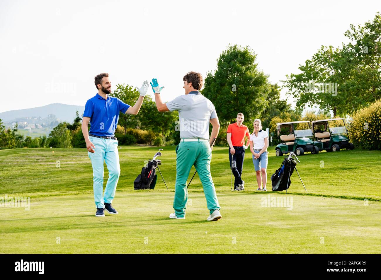 Freunde, die hohe fünf auf dem Golfplatz geben, Paare beobachten im Hintergrund Stockfoto
