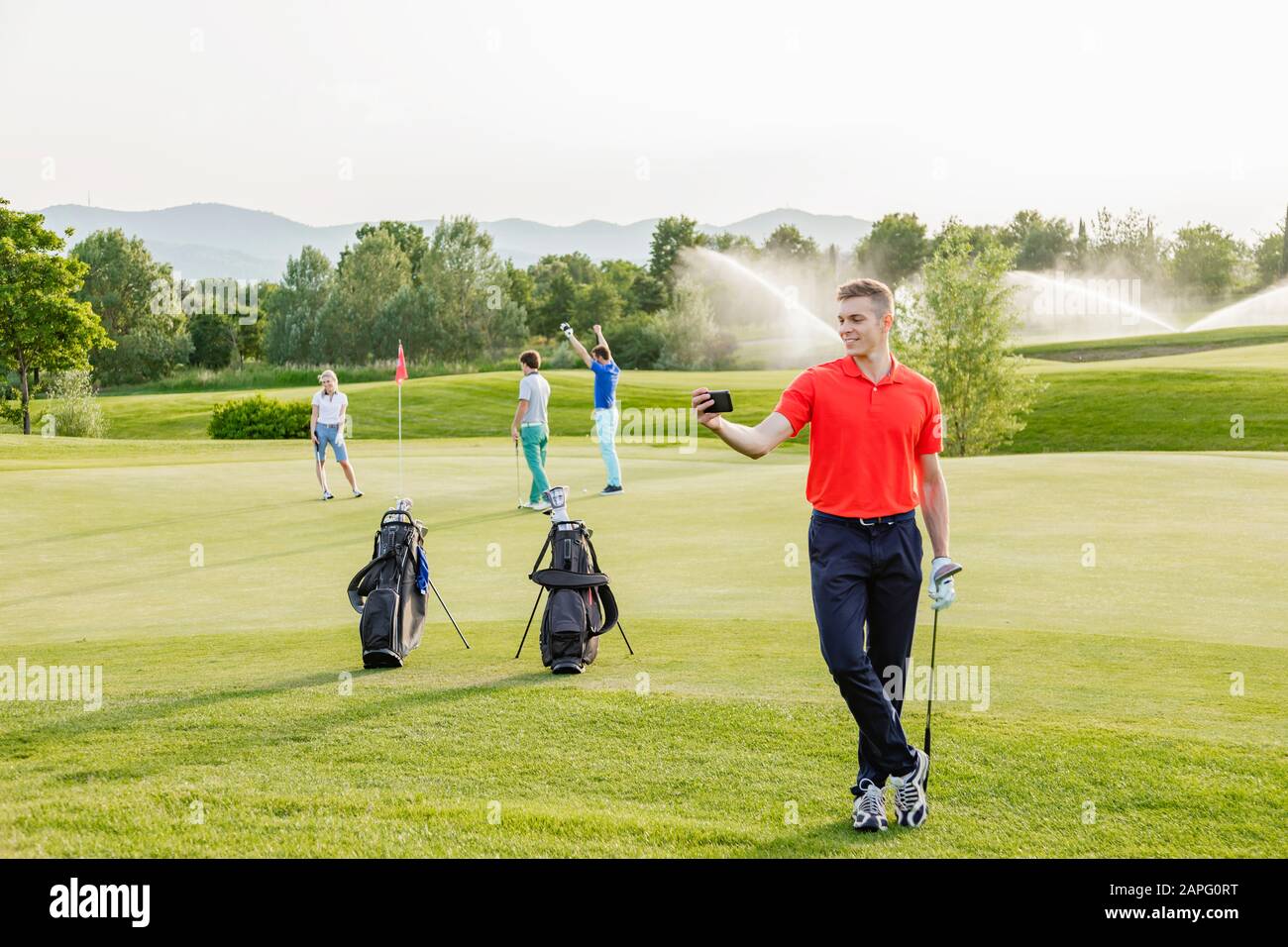 Mann, der selfie auf dem Golfplatz nimmt, Freunde, die im Hintergrund Golf spielen Stockfoto