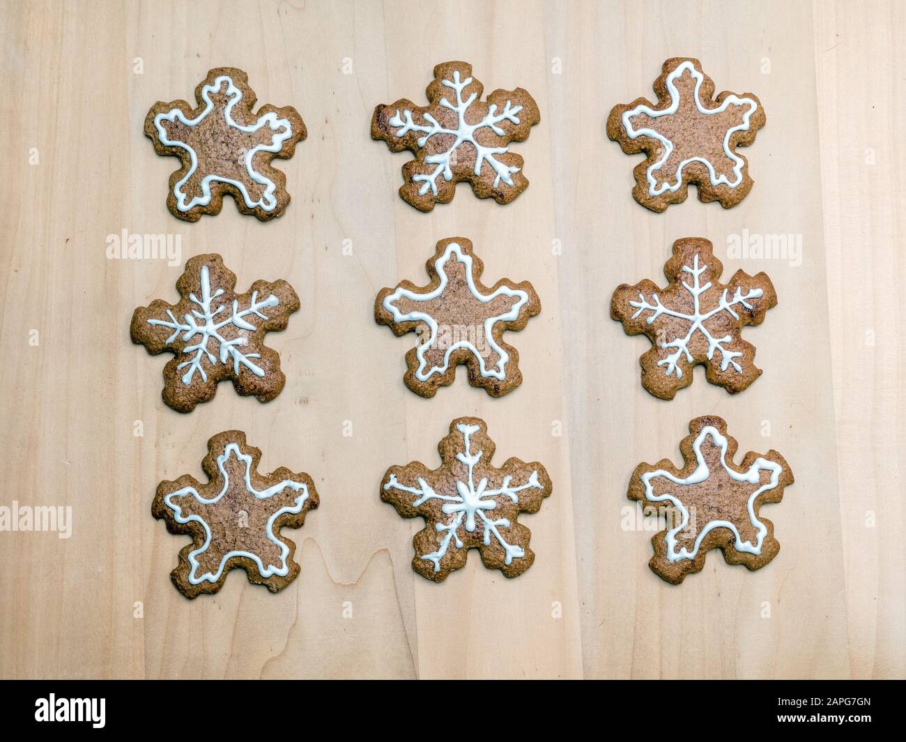 Weihnachts-Lebkuchen-Kekse in Schneeflockenform mit weißer Vereisung, die auf rustikalem Holzbrett angeordnet ist, von oben beschossen Stockfoto