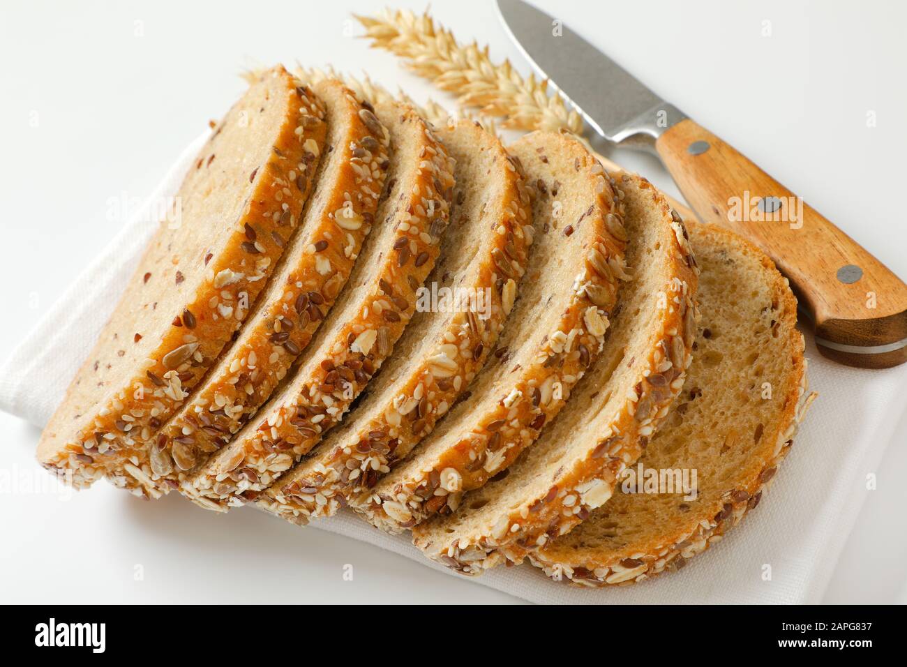 Brotlaib aus Vollkornbrot auf weißer Serviette, Weizenähren und Küchenmesser daneben Stockfoto
