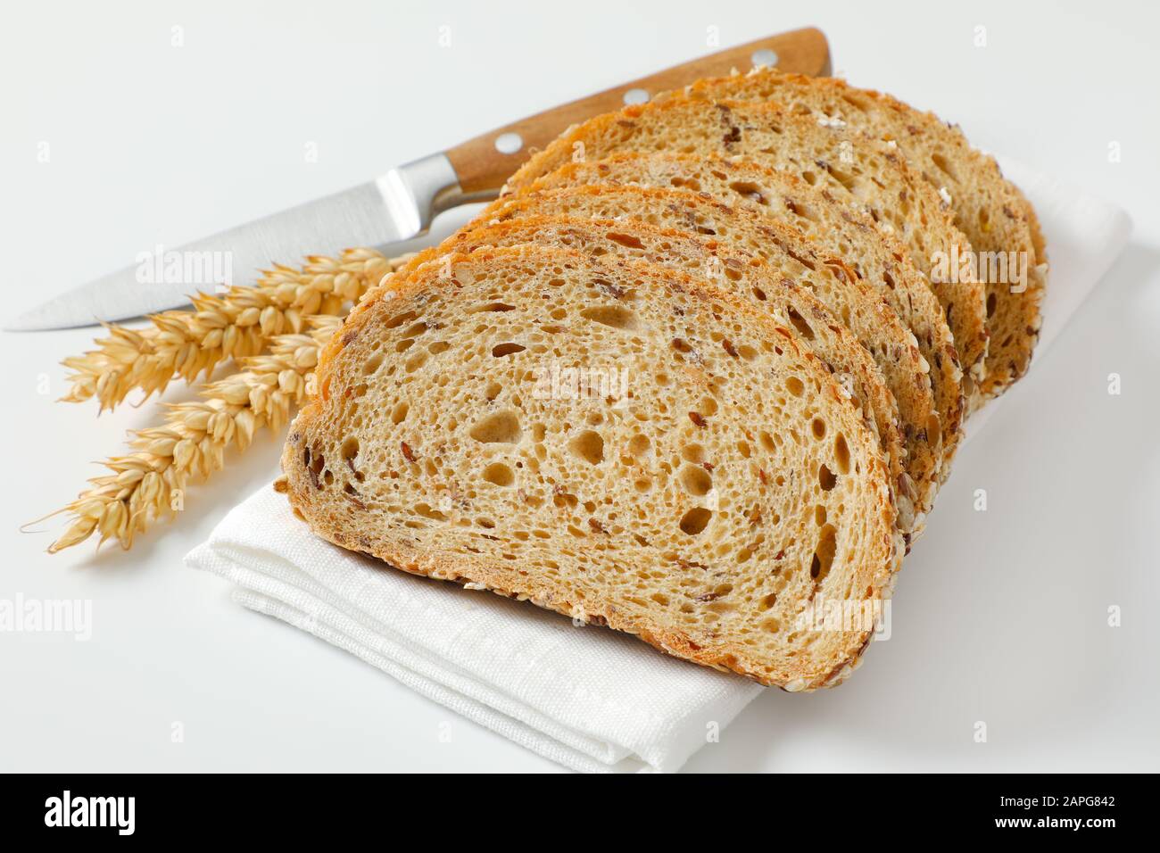 Brotlaib aus Vollkornbrot auf weißer Serviette, Weizenähren und Küchenmesser daneben Stockfoto