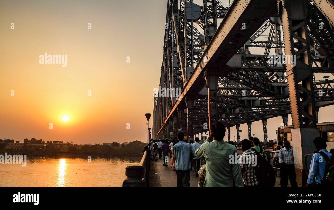 Blick über den Hooghly River an der untergehenden Sonne wie Scharen von Menschen und Verkehr über die Brücke hin und her. Stockfoto