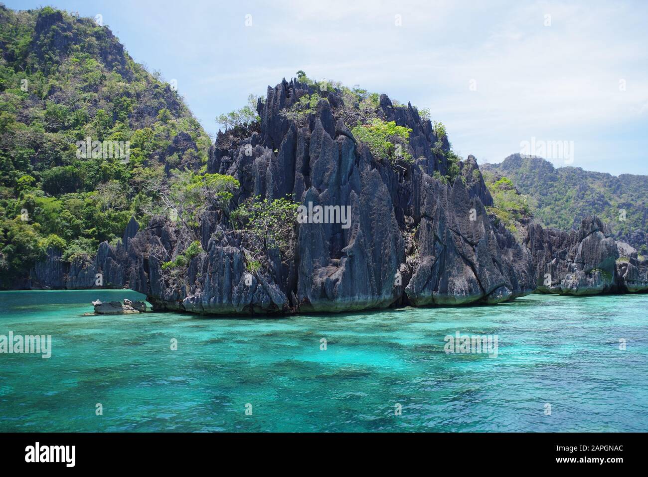 Ein großer, zerklüftter Felsen, der in der Nähe einer der Inseln auf den Philippinen aus dem Meer ragt. Spärlich bedeckt von Schrubbern und von einem kleinen Riff umgeben. Stockfoto